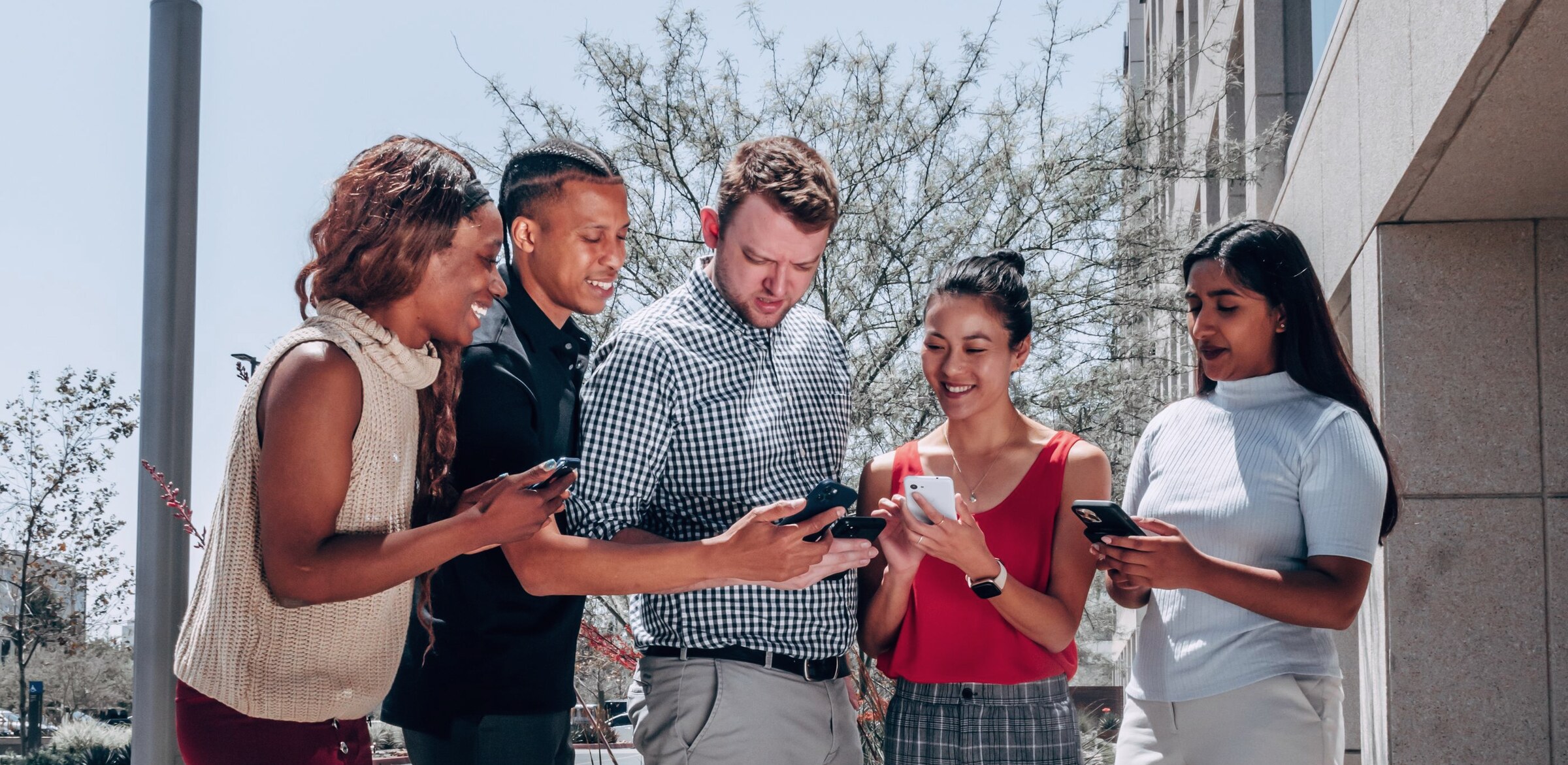 Five colleagues outside an office building, each using their own work mobile