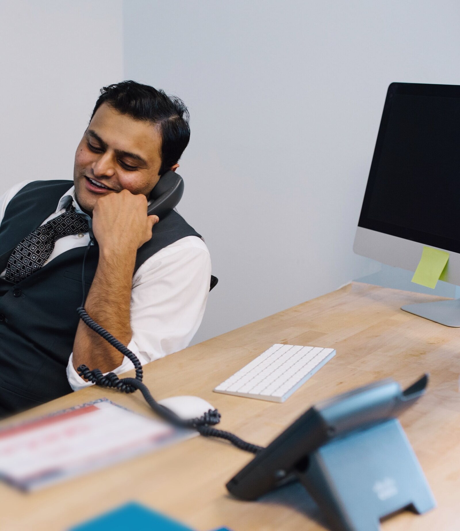 A man laughing on a desk phone call at his desk