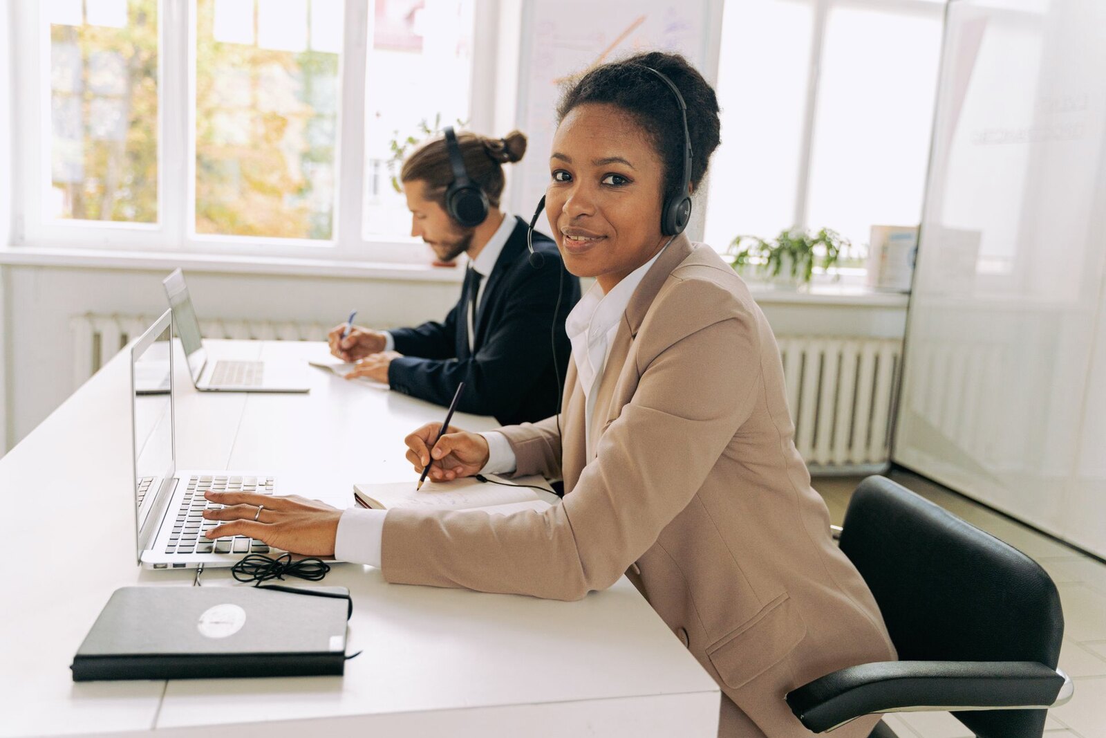 Two colleagues on headset calls at their desks in a bright office