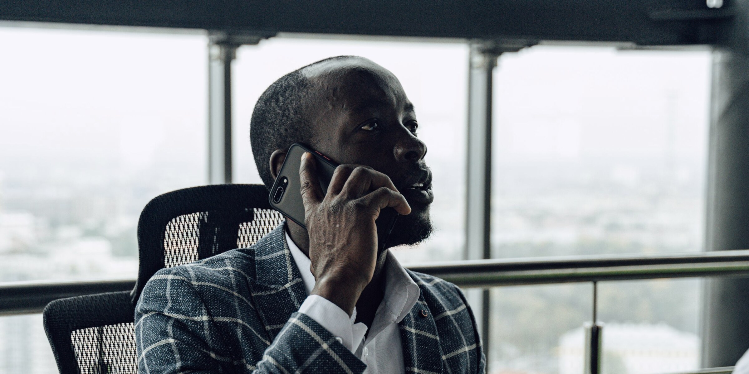 A businessman taking a call at his desk by a window over the city