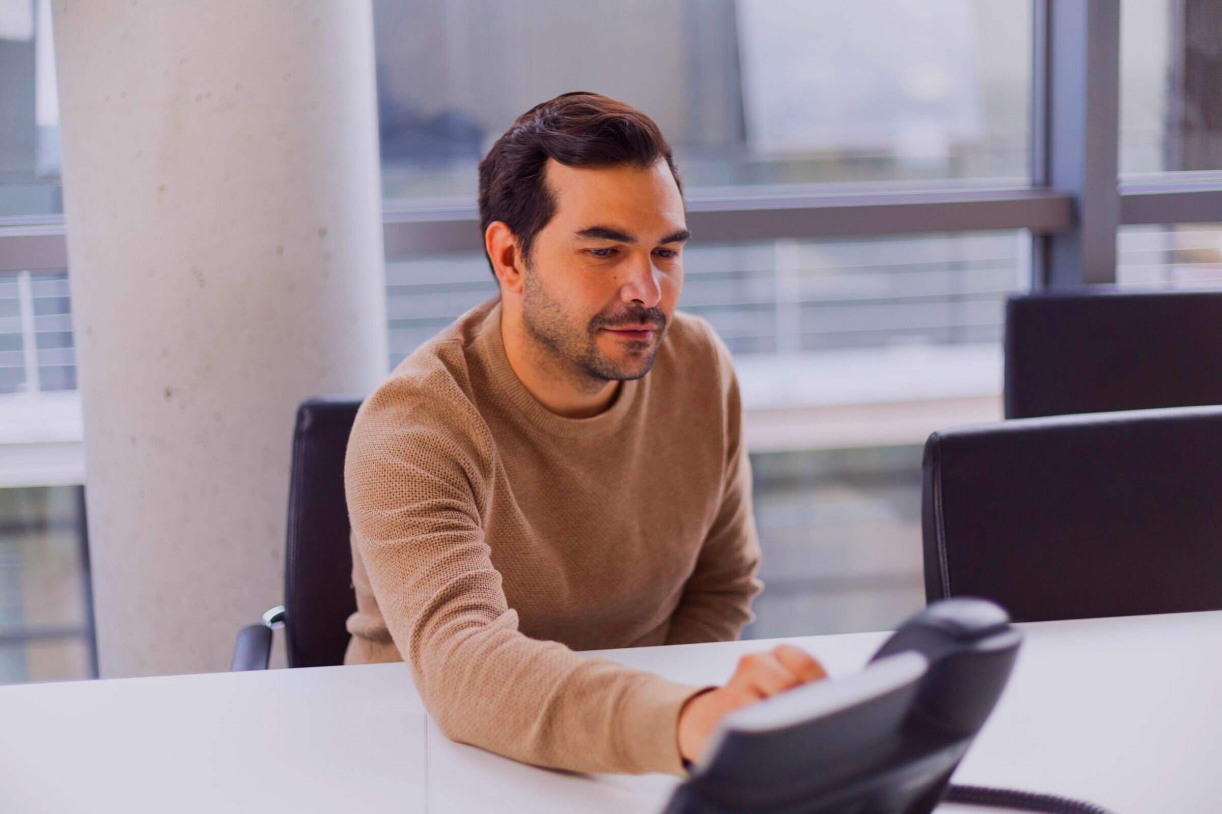 A man answering a desk phone in a bright office