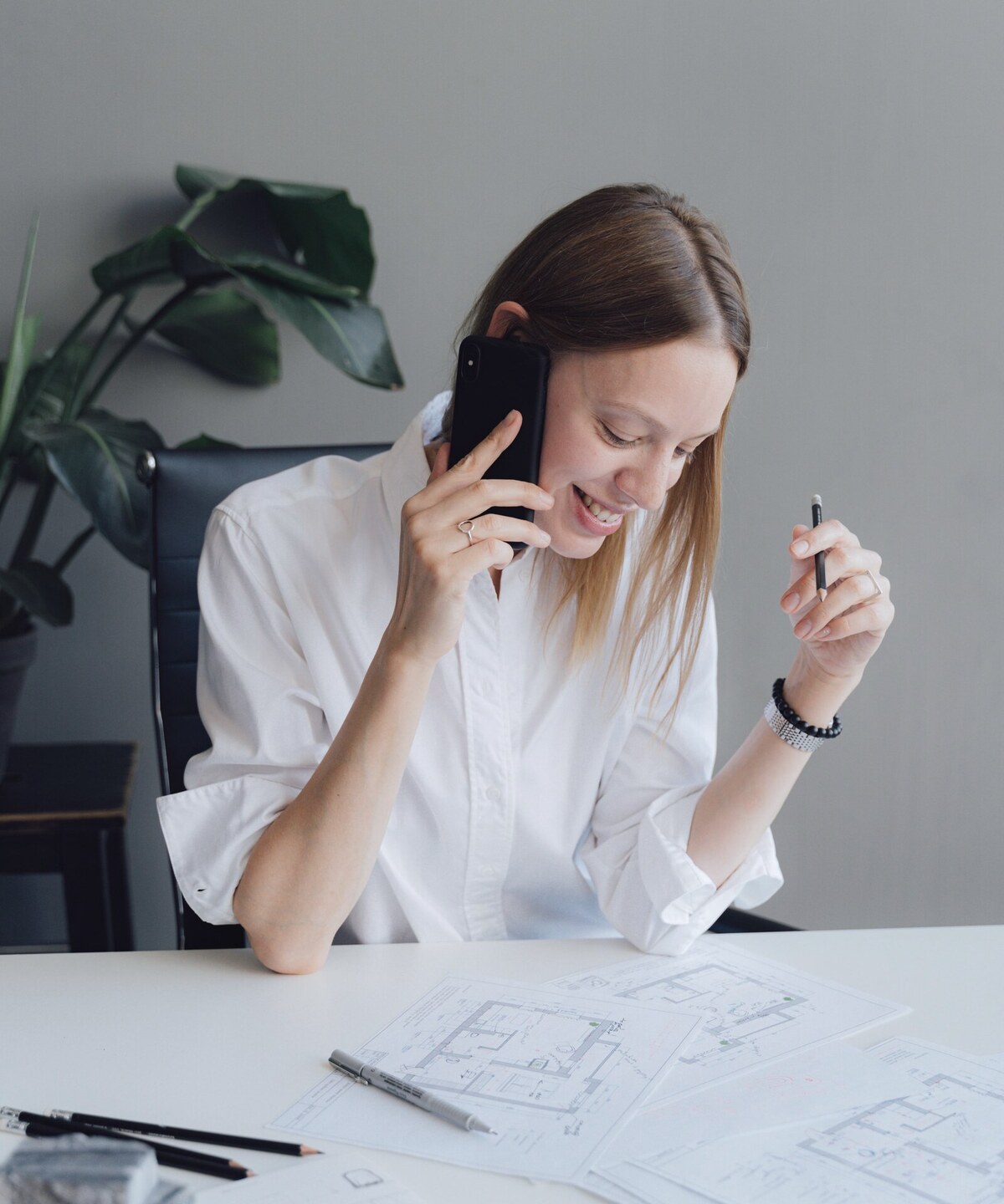 A woman on a mobile call at her desk, working on drawings
